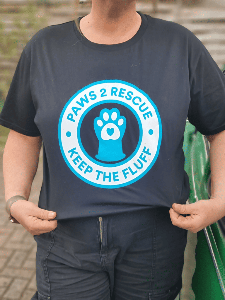 A photo of a limited edition t-shirt with a circular logo containing a dogs paw and the words "Paws2Rescue, keep the fluff" printed on the front.
