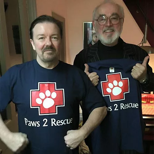 A photo of Ricky Gervais and Peter Egan both wearing t-shirts with the Paws2Rescue logo printed on the front